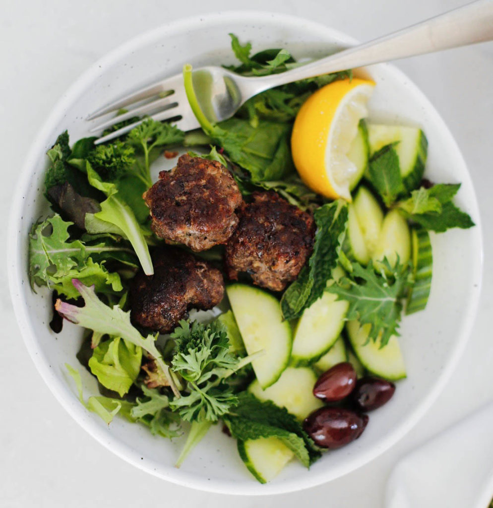 Lamb meatballs on top of a green salad with olives, cucumber and lemon