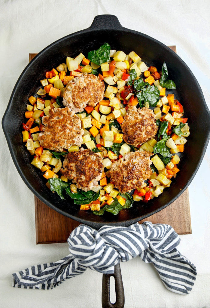 Pork breakfast sausage in a cast iron pan with root vegetables and spinach