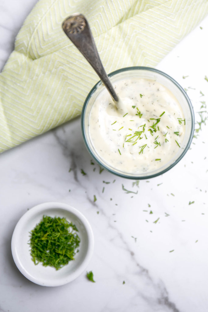 Ranch dressing in a cup with a spoon and fresh dill