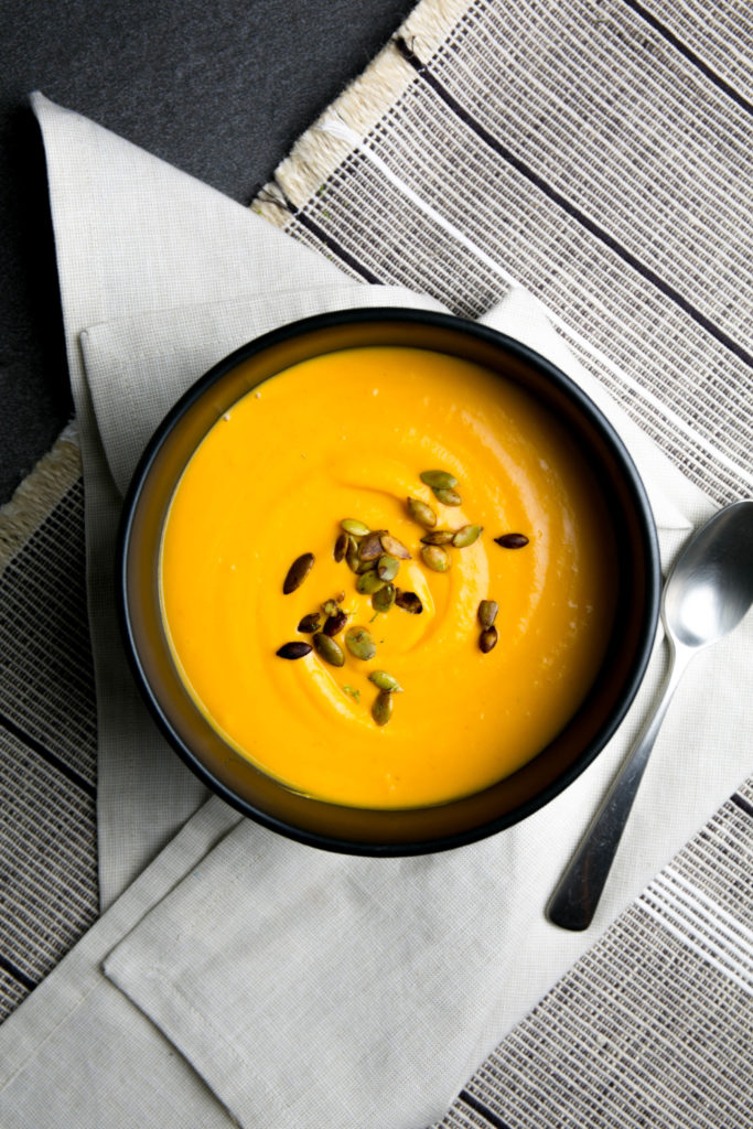 Sweet potato coconut curry soup in a black bowl with pumpkin seeds on top