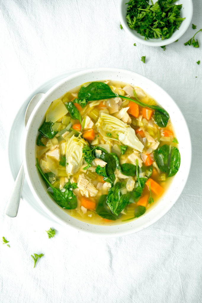 A bowl of chicken, lemon and artichoke soup with parsley and a spoon