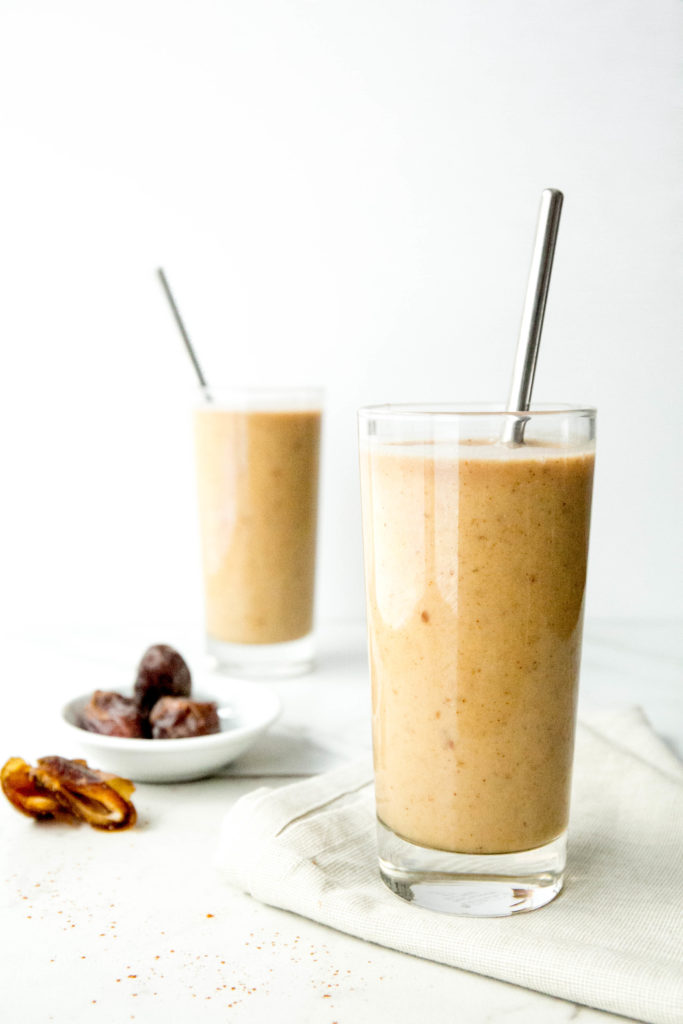 Two chai charger smoothies in glasses with straws and a bowl of dates