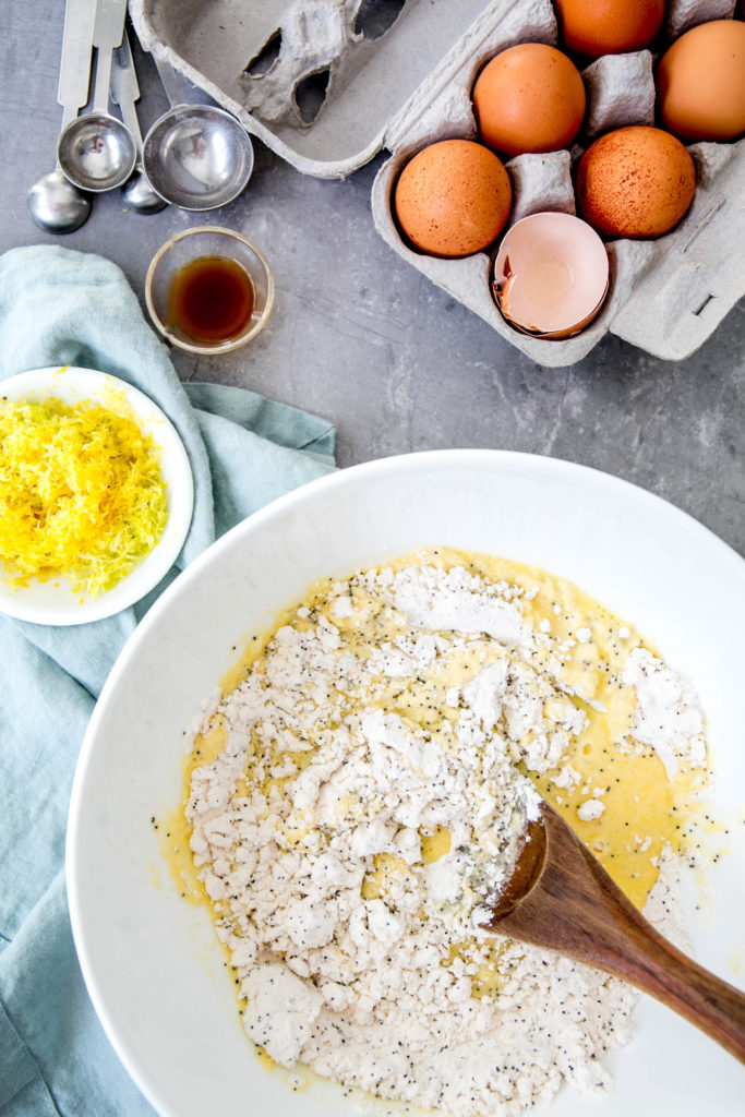 Pancake batter in a bowl with spoon, eggs, lemon zest and vanilla extract