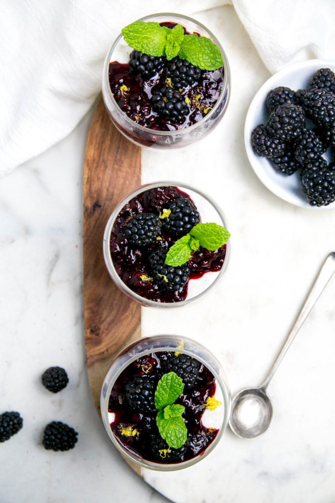 Three glass jars of vanilla bean panna cotta with blackberries and mint