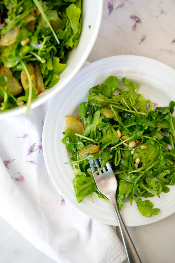 a plate of arugula and potato salad with chive blossoms and a fork