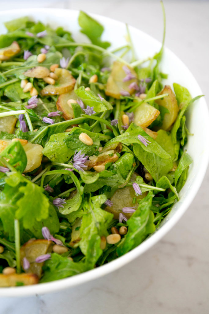 a bowl of arugula and potato salad with pine nuts, and chive blossoms 