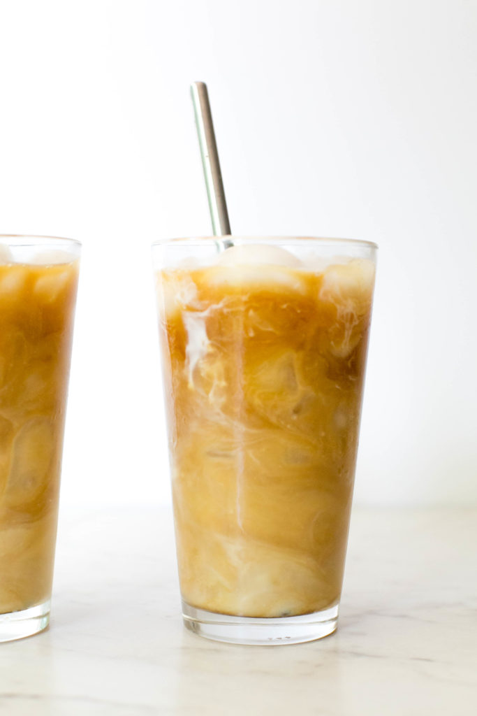 A glass full of ice with iced coffee and a straw