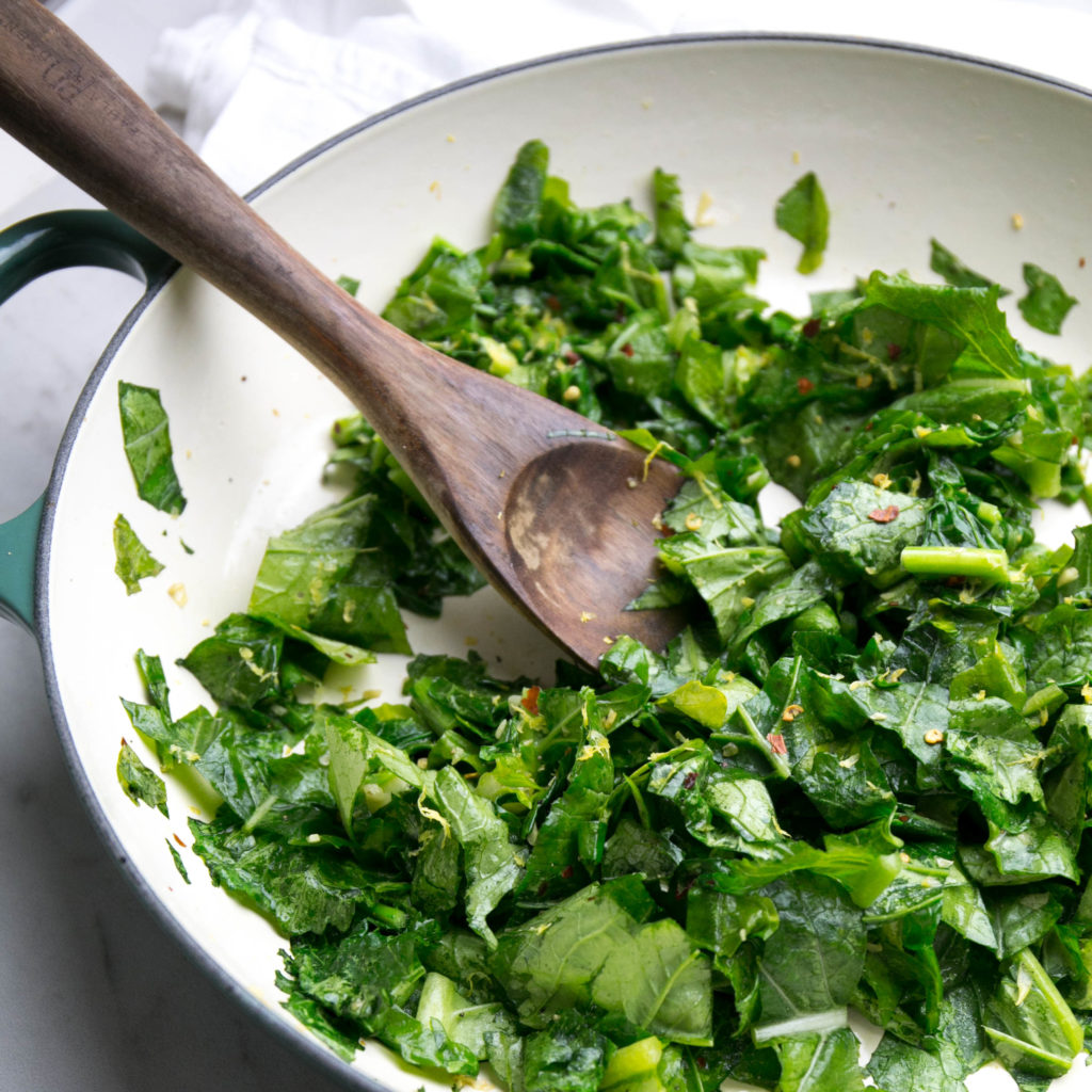 sautéed rapini in a skillet with a wooden spoon