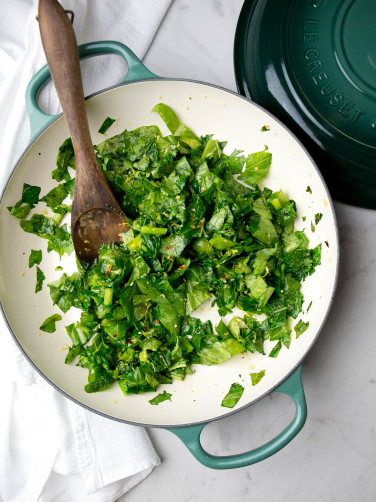 sautéed rapini in a skillet with a lid and wooden spoon