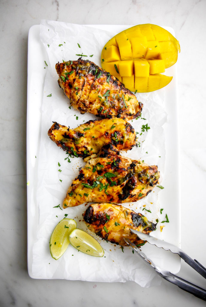 grilled mango lime chicken on a platter with limes, mango and tongs