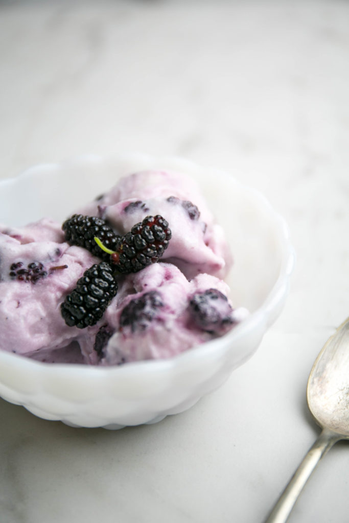 mulberry ice cream in a bowl with fresh mulberries and a spoon