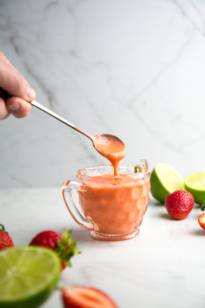 strawberry lime vinaigrette dripping off a spoon with cut up strawberries and limes