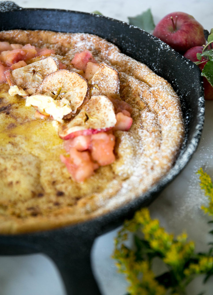 Side view of an apple cinnamon dutch baby with apple sauce, apples and maple syrup