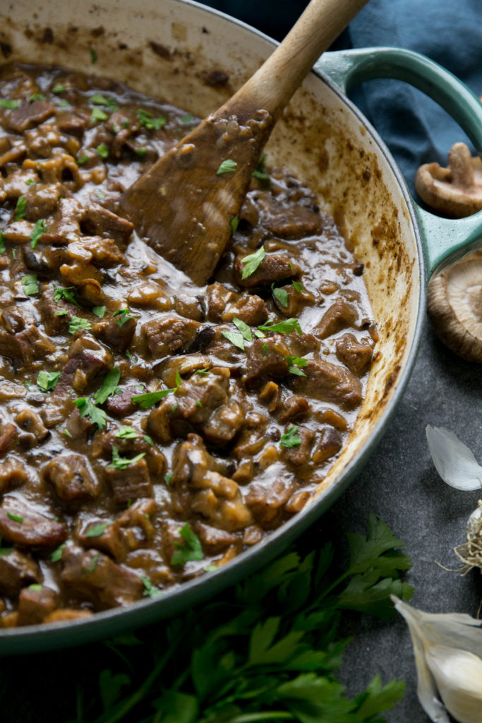 Beef stroganoff in a skillet with a wooden spatula and mushrooms, garlic and parsley