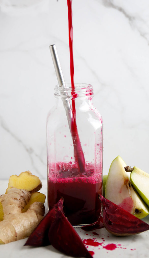 Beet, pear and ginger juice being poured into a glass with a stainless steel straw 