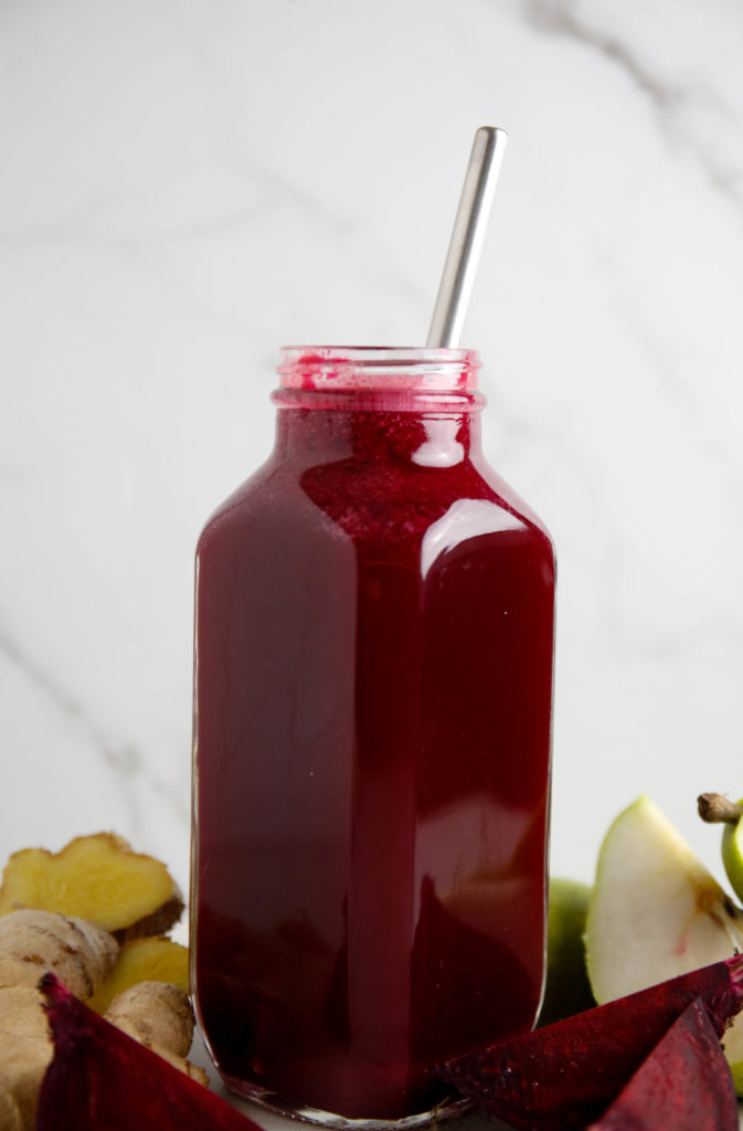glass of beet, pear and ginger juice with a stainless steel straw