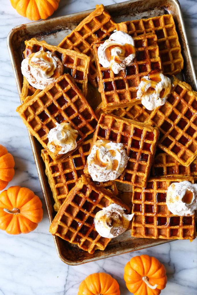 Aerial view of pumpkin spice waffles on a sheet tray with pumpkins and whipped cream