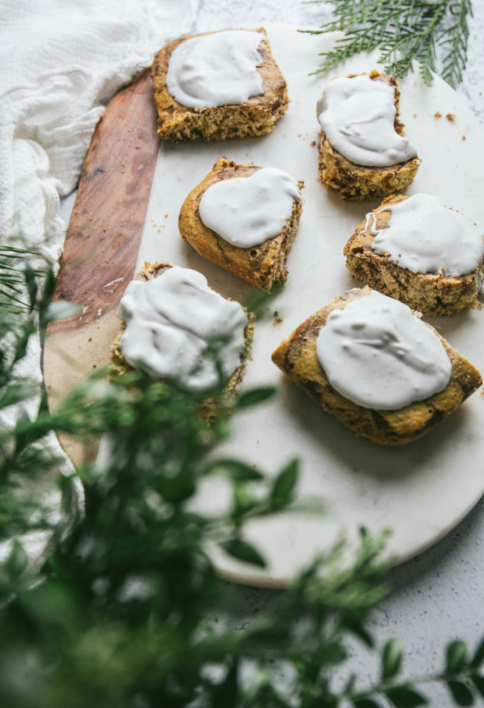 A view of grain free cinnamon rolls with frosting behind some pine needles