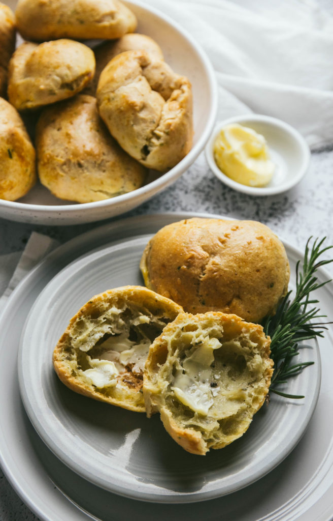 Aerial view of a rosemary garlic dinner roll on a plate with butter and a fresh sprig of rosemary