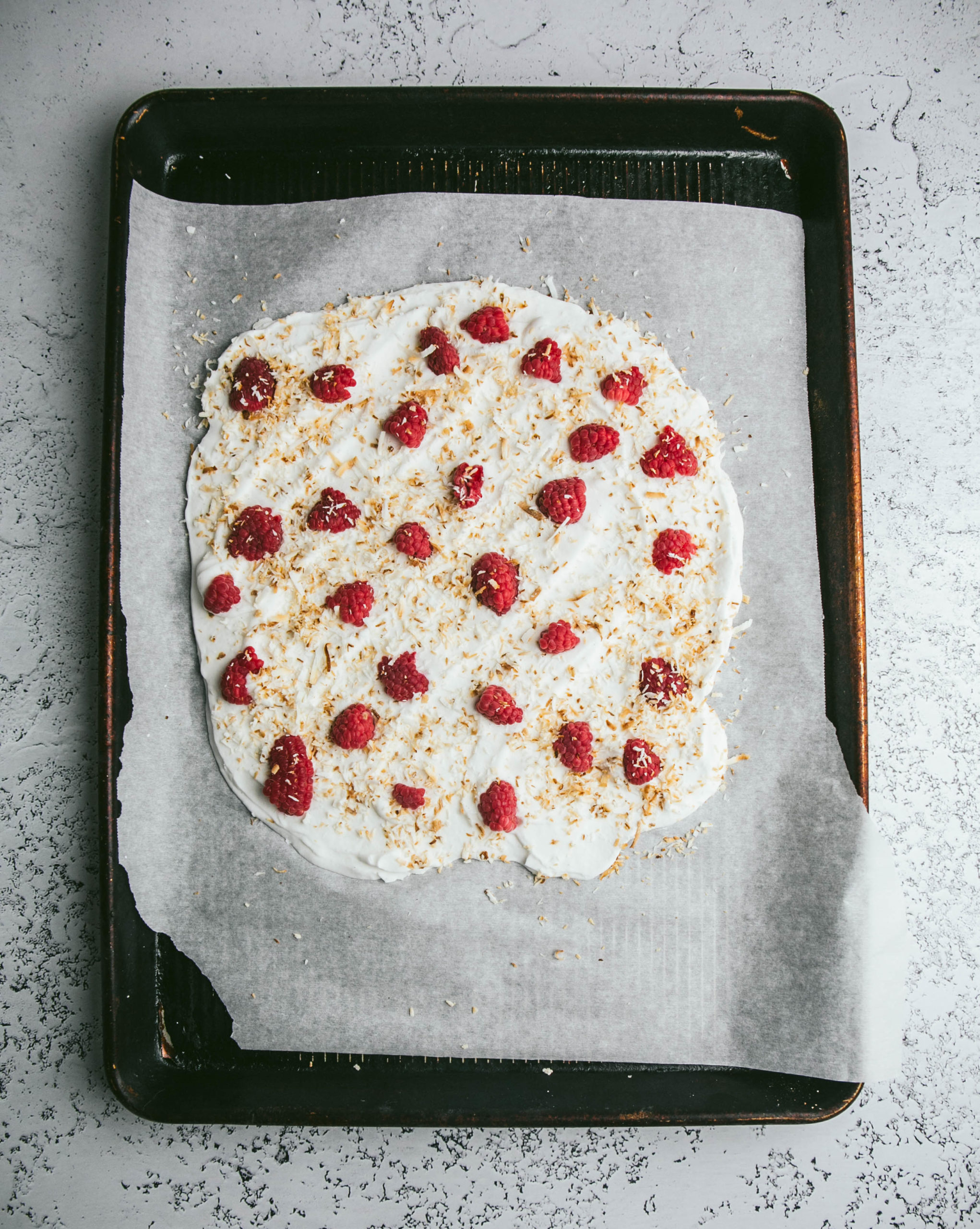 Yogurt spread out on baking tray with raspberries and toasted coconut