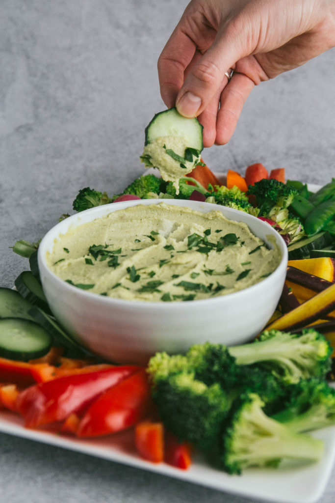 A cucumber being dipped into Vegan French Onion Dip with other vegetables