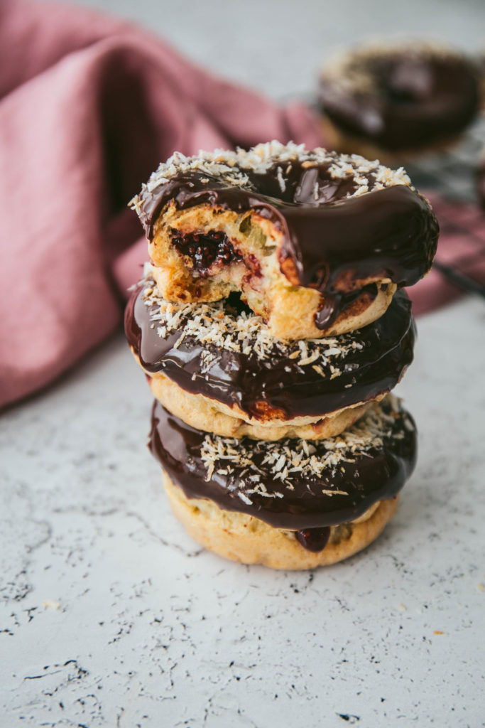 Three grain-free donuts with raspberry filling and chocolate glaze stacked on top of each other