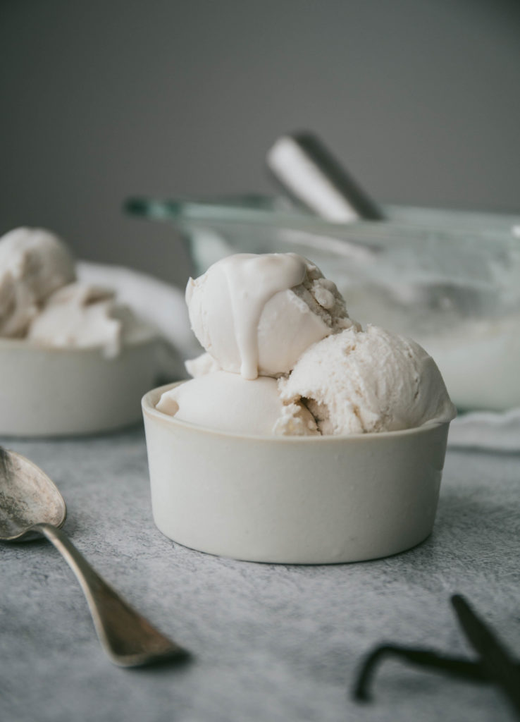 dairy-free vanilla ice cream in a dish with a spoon and vanilla beans