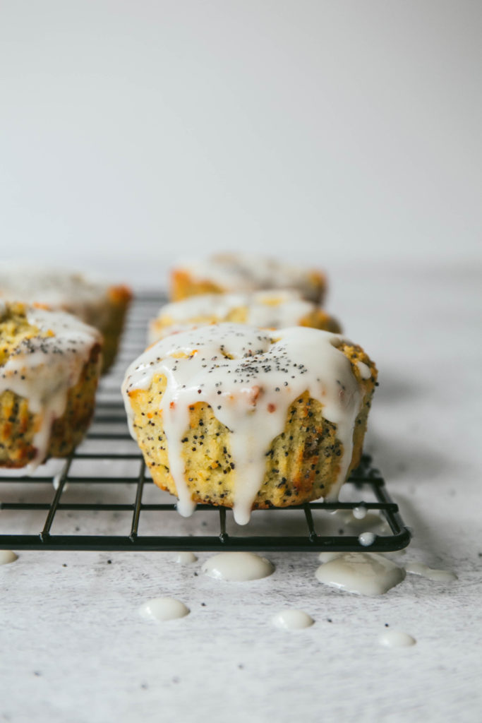 Lemon poppyseed muffins on a cooling rack with lemon coconut glaze and poppyseed on top