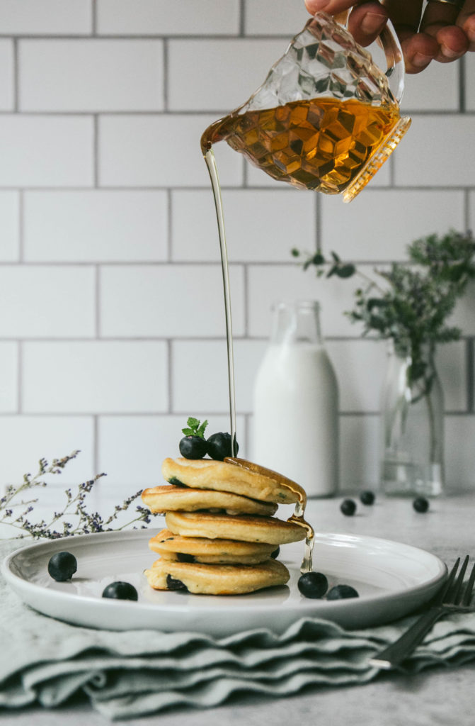 Mini blueberry pancakes with maple syrup being drizzled on top