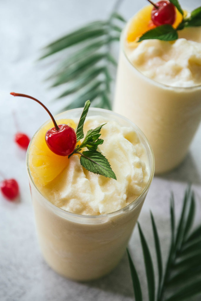 Two virgin pina coladas with pineapple and cherry garnishes