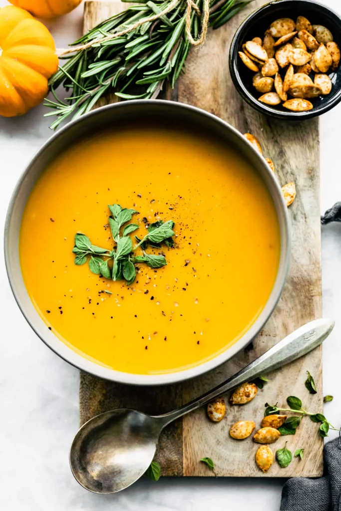 Instant pot butternut squash soup with apple in a bowl with pumpkin seeds and fresh rosemary