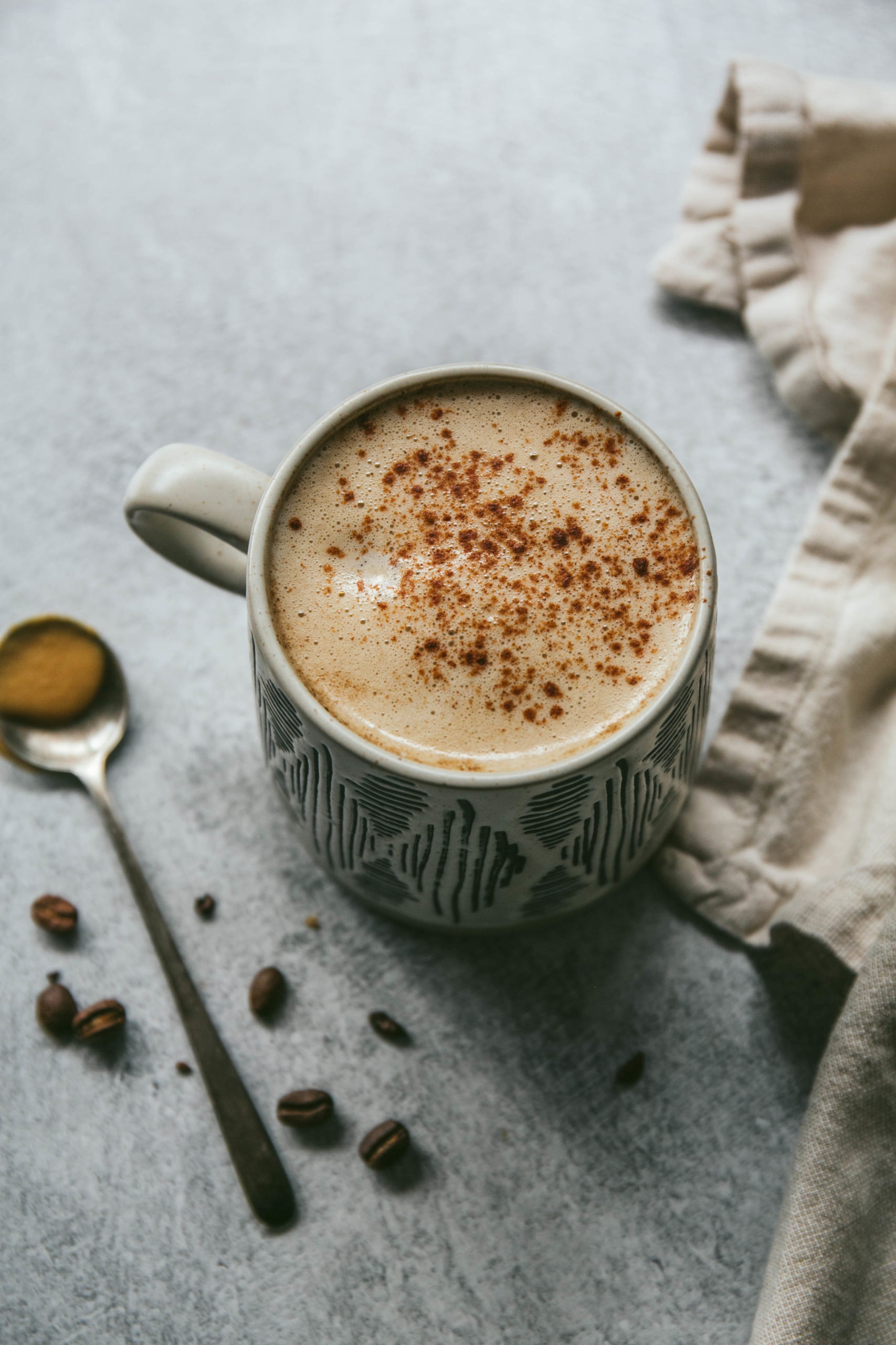 Aerial view of maple tahini latte with a spoon of tahini and coffee beans