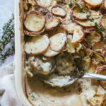 Aerial view of dairy-free scalloped potatoes with a serving spoon and fresh thyme