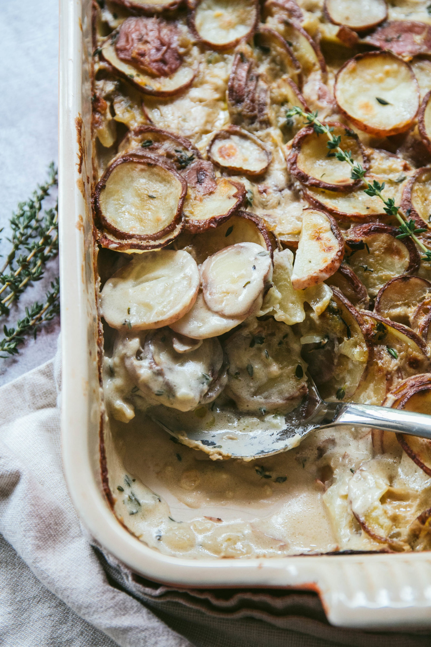 Aerial view of dairy-free scalloped potatoes with a serving spoon and fresh thyme