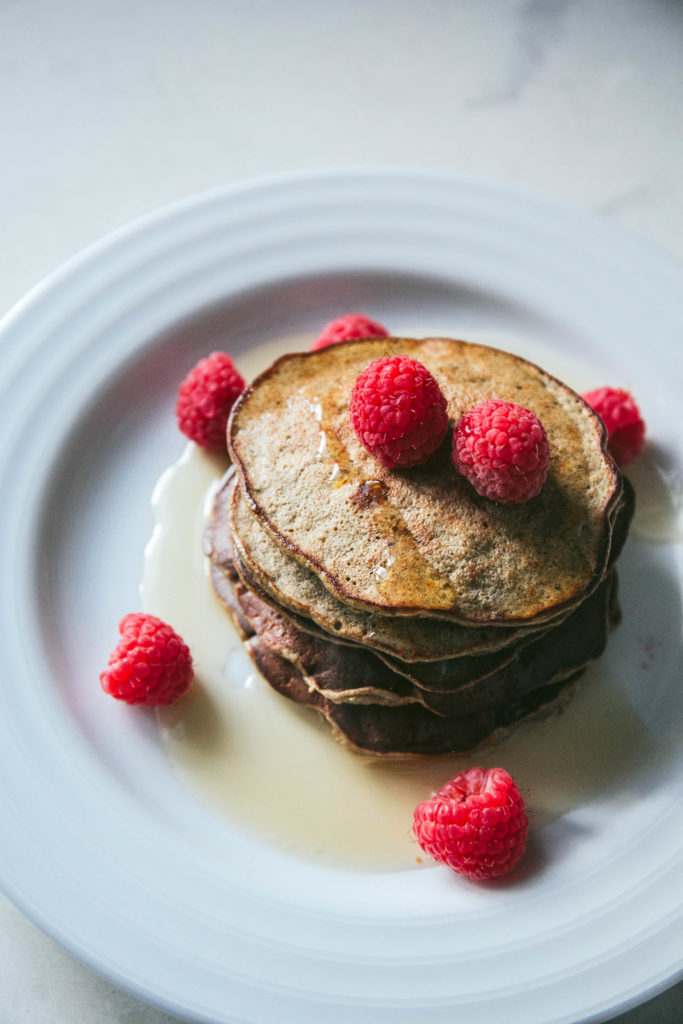 Protein pancakes on a plate with maple syrup and raspberries