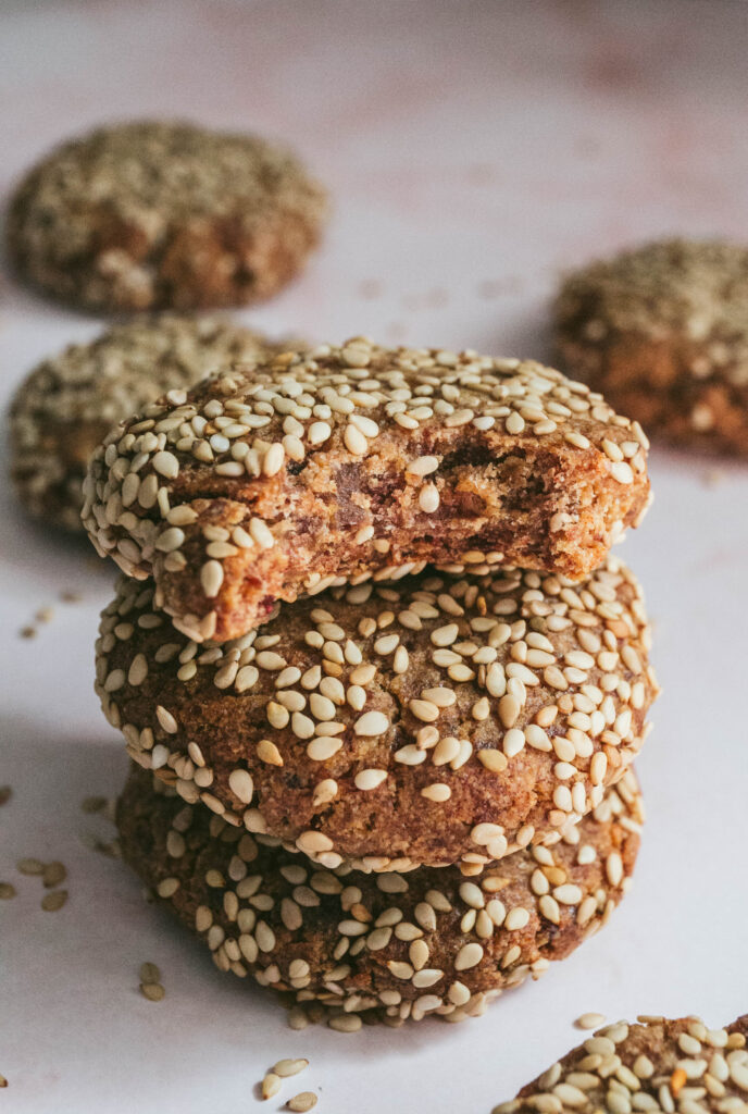 Vegan date and tahini cookies stacked on top of each other with sesame seeds