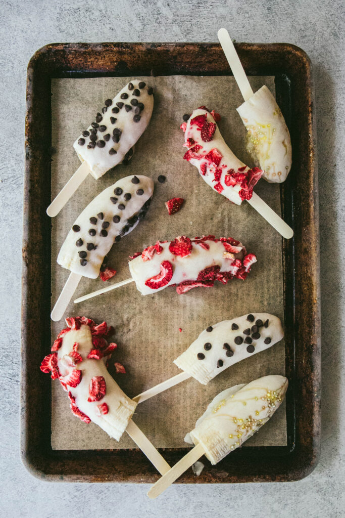 Frozen yogurt banana pops on a baking tray with toppings
