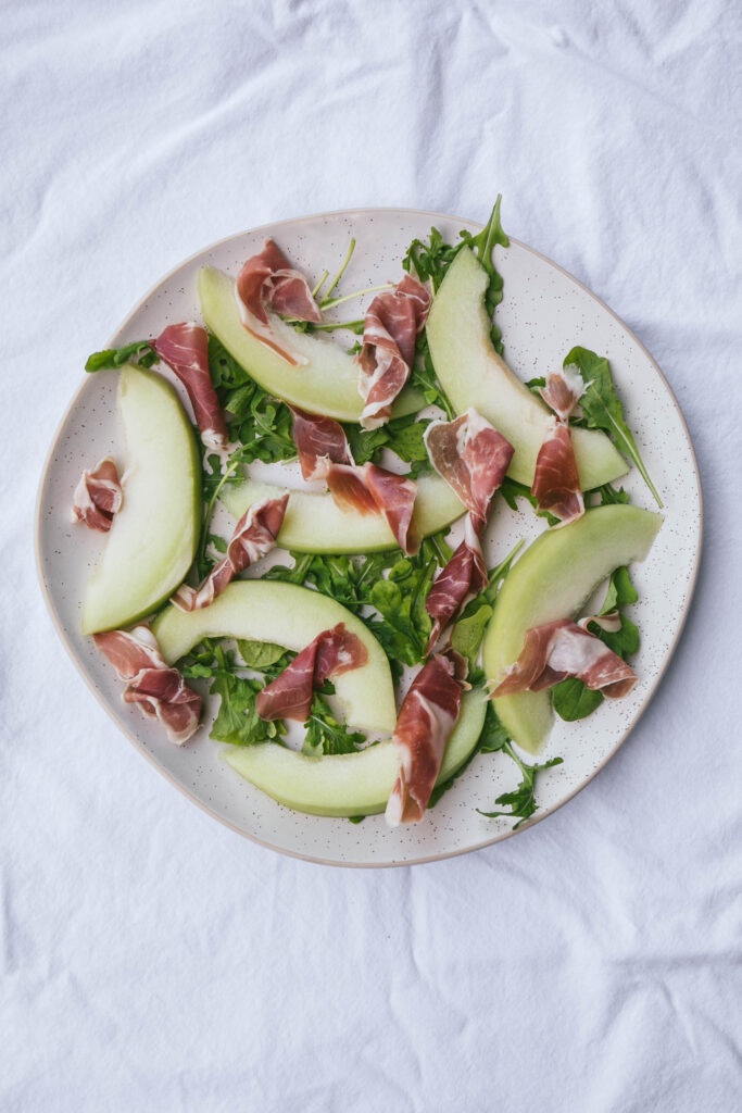 Honeydew melon and prosciutto on a platter with arugula