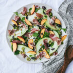 Prosciutto and melon appetizer on a platter with napkin and serving spoons