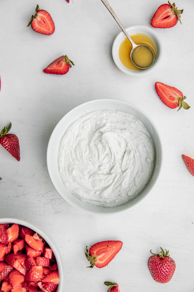 Coconut whipped cream in a bowl with honey and fresh strawberries