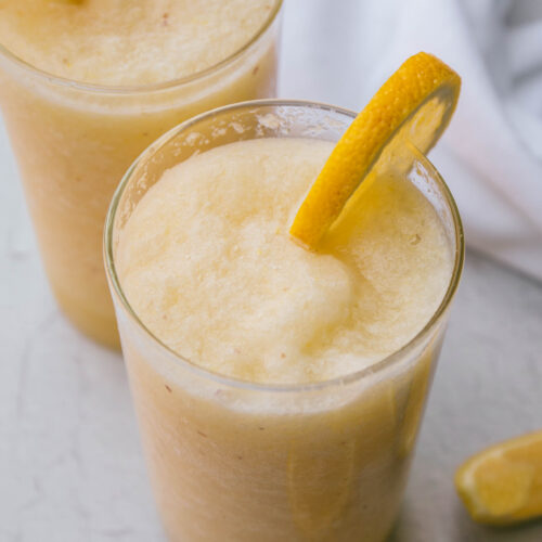Two frozen lemonades with fresh lemon on the rim of the glass