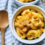 Pumpkin mac and cheese in a bowl with a wooden spoon on the side